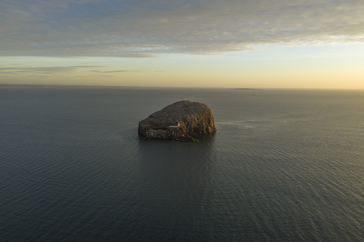 Aerial view of Bass Rock Lighthouse on a steep volcanic island surrounded by the calm sea under a golden sunset sky North Berwick Scotland United Kingdom. Aerial view of Bass Rock Lighthouse on a steep volcanic island surrounded by the calm sea under a golden sunset sky North Berwick Scotland United Kingdom.