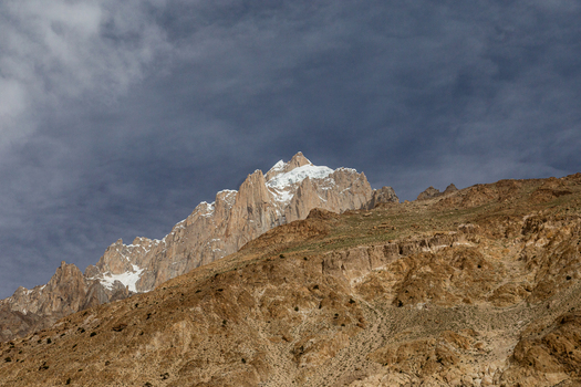 View of Baltoro Glacier with snow capped peaks rising above rugged rocky slopes under a dramatic cloudy sky in Baltoro Gilgit Baltistan Pakistan.