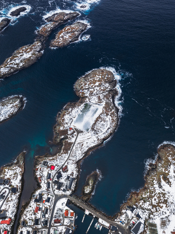 Aerial view of snow dusted islands meet the frigid sea a tapestry of white and deep blue contrasting with the quaint village below Henningsv&aelig;r Nordland Norway.