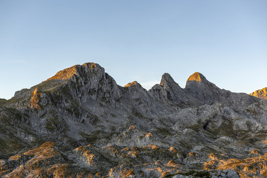 View of rugged sunlit mountain peaks piercing the clear blue sky creating a dramatic contrast of light and shadow on the rocky landscape Picos de Europa Asturias Spain.