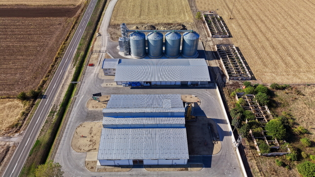 Aerial view of the storage silo Bavaniste featuring metal grain silos and warehouse buildings in a paved industrial yard surrounded by agricultural fields in Bavaniste Vojvodina Serbia.