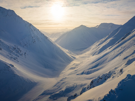 Aerial view of the Arctic National Wildlife Refuge featuring snow covered mountain peaks and a deep valley under the low winter sun in Alaska United States.