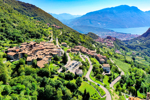 Aerial view of the historic stone village of Canale di Tenno nestled among lush green mountains with Lake Garda in the background Ville del Monte Trentino Alto Adige Italy. Aerial view of the historic stone village of Canale di Tenno nestled among lush green mountains with Lake Garda in the background Ville del Monte Trentino Alto Adige Italy.