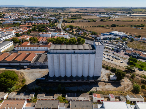 Aerial view of the large white grain silo situated in an industrial area with surrounding buildings roads and agricultural fields in Evora Evora District Portugal. Aerial view of the large white grain silo situated in an industrial area with surrounding buildings roads and agricultural fields in Evora Evora District Portugal.