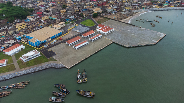 Aerial view of the Elmina fishing harbor with traditional wooden boats anchored in the bay modern port facilities and the historic townscape in Elmina Central Region Ghana. Aerial view of the Elmina fishing harbor with traditional wooden boats anchored in the bay modern port facilities and the historic townscape in Elmina Central Region Ghana.