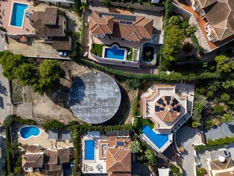 Aerial view of residential villas with swimming pools and a large circular water reservoir surrounded by lush greenery in Moraira Valencian Community Spain.