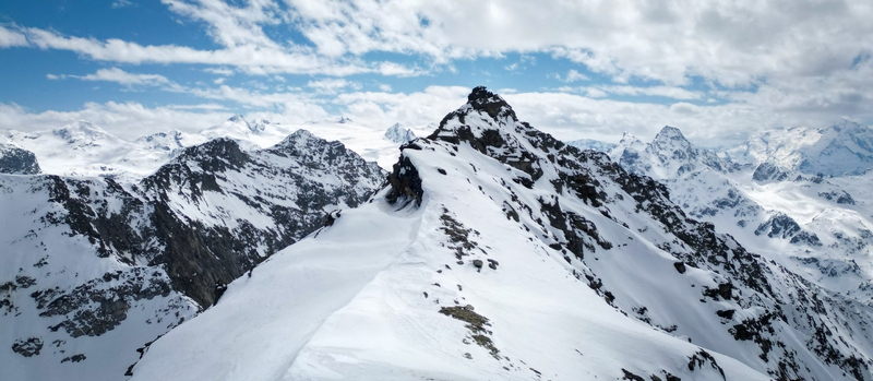 Aerial view of snow capped peaks under a sky of scattered clouds the crisp white meeting the rugged dark rock faces Arpy Valle d Aosta Italy. Aerial view of snow capped peaks under a sky of scattered clouds the crisp white meeting the rugged dark rock faces Arpy Valle d Aosta Italy.