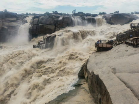 View of Augrabies Falls with powerful torrents of water plunging into the rocky gorge mist rising and visitors on the observation deck in Augrabies Northern Cape South Africa.