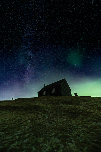 View of a solitary house silhouetted against the ethereal glow of the Aurora Borealis under a star studded sky Krysuvikurkirkja Hafnarfjardarkaupstadur Iceland.