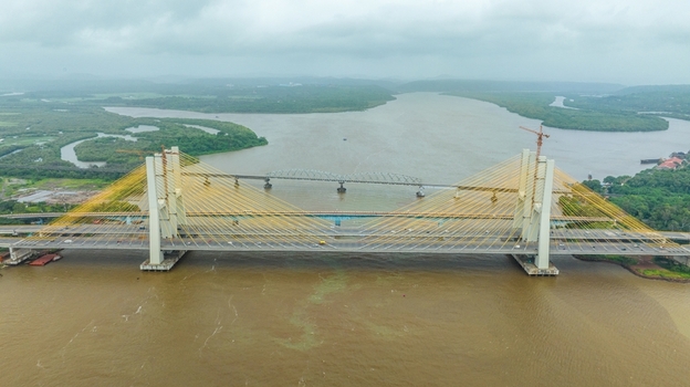 Aerial view of the Zuari Bridge spanning the Zuari River with cable stayed design lush green riverbanks and cloudy sky in Cortalim Goa India.