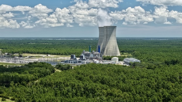 Aerial view of the Seminole Electric Cooperative power plant with cooling towers emitting steam surrounded by dense forest under a blue sky in Palatka Florida United States.