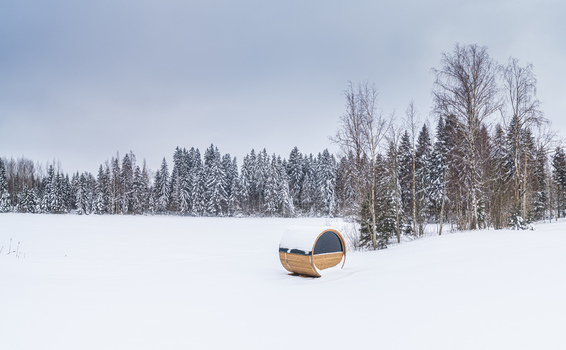 Aerial view of a wooden barrel sauna sitting in a vast snow covered field with a dense forest of snow dusted pine trees in the background in Latvia. Aerial view of a wooden barrel sauna sitting in a vast snow covered field with a dense forest of snow dusted pine trees in the background in Latvia.