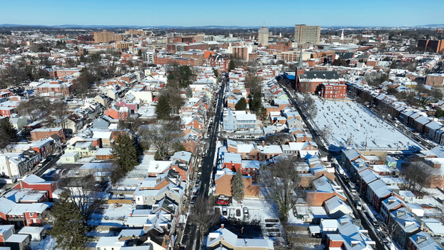 Aerial view of the historic city of Lancaster blanketed in snow featuring brick rooftops a prominent church and a cemetery under a clear blue sky in Lancaster Pennsylvania United States.