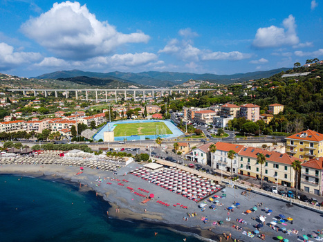 Aerial view of the sandy coastline with beach umbrellas a sports stadium and a large highway viaduct against green hills in Imperia Liguria Italy. Aerial view of the sandy coastline with beach umbrellas a sports stadium and a large highway viaduct against green hills in Imperia Liguria Italy.