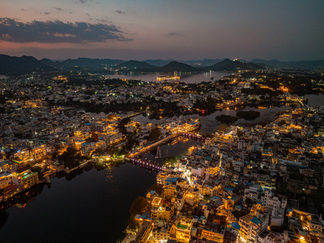 Aerial view of the illuminated cityscape of Udaipur at night featuring historic architecture and bridges reflecting over Lake Pichola under a twilight sky Udaipur Rajasthan India.