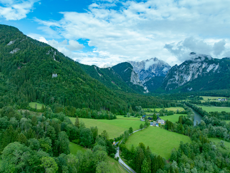Aerial view of Nationalpark Gesause with a winding river flowing through a lush green valley scattered houses and dramatic mountain peaks such as Hochtor in Admont Steiermark Austria.