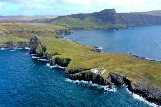 Aerial view of Neist Point Lighthouse on the dramatic cliffs of the Isle of Skye surrounded by the deep blue Atlantic Ocean and green hills. Isle of Skye Scotland United Kingdom.