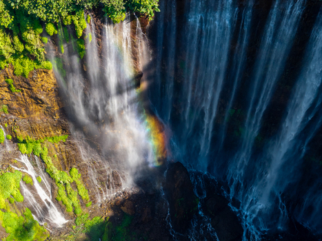 Aerial view of Tumpak Sewu Waterfall cascading down lush green cliffs with a vibrant rainbow in the mist Kecamatan Pronojiwo Jawa Timur Indonesia.