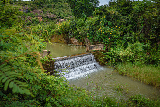 View of Lamingo Dam with water cascading over the concrete weir surrounded by lush green vegetation and rocky hills in Jos Plateau Nigeria.