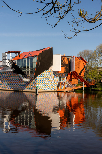 Groningen Netherlands 23 April 2024 View of the Groninger Museum with its colorful tiled facade and modern orange structures reflecting in the canal water under a clear blue sky. Groningen Netherlands 23 April 2024 View of the Groninger Museum with its colorful tiled facade and modern orange structures reflecting in the canal water under a clear blue sky.