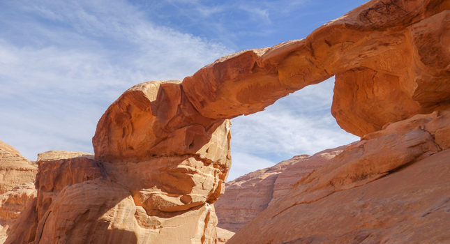 View of the natural sandstone rock bridge in the Wadi Rum Desert featuring rugged red rock formations under a clear blue sky in Wadi Rum Village Aqaba Governorate Jordan. View of the natural sandstone rock bridge in the Wadi Rum Desert featuring rugged red rock formations under a clear blue sky in Wadi Rum Village Aqaba Governorate Jordan.