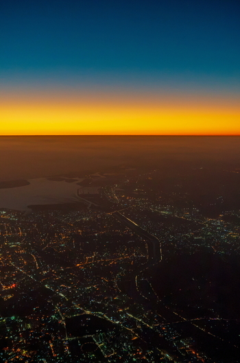Aerial view of the sprawling city lights of Karachi at dusk with the coastline visible against a vibrant sunset horizon in Karachi Sindh Pakistan.