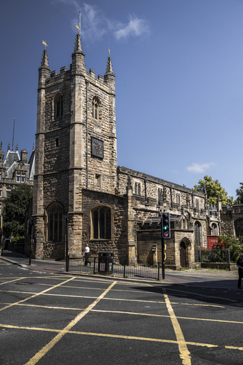 View of the historic St John the Baptist Church with its stone clock tower and gothic windows situated at a street intersection in Newcastle upon Tyne England United Kingdom. View of the historic St John the Baptist Church with its stone clock tower and gothic windows situated at a street intersection in Newcastle upon Tyne England United Kingdom.