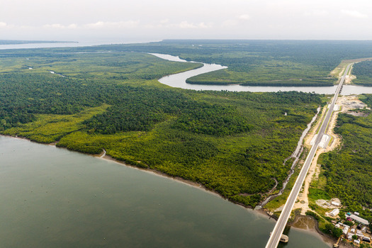 Aerial view of a long bridge spanning a wide river through dense mangrove forests and lush green vegetation under a cloudy sky in Opobo Town Rivers Nigeria. Aerial view of a long bridge spanning a wide river through dense mangrove forests and lush green vegetation under a cloudy sky in Opobo Town Rivers Nigeria.