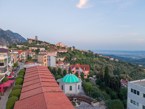 Aerial view of the historic Kruje Castle perched on a rocky hill overlooking red tiled rooftops and a green domed building under a clear sky in Kruje Durres County Albania.