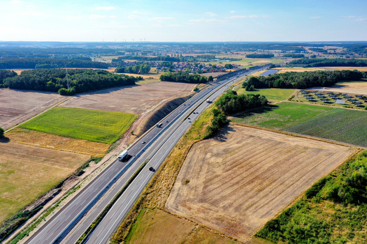 Aerial view of a highway with cars and trucks passing through green fields and dense forests under a clear blue sky Hochstadt Bavaria Germany. Aerial view of a highway with cars and trucks passing through green fields and dense forests under a clear blue sky Hochstadt Bavaria Germany.