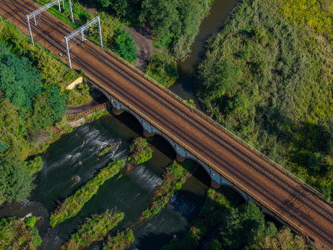 Aerial view of a railway bridge crossing a river with lush green vegetation and trees along the banks in Sosnowiec Wojewodztwo slaskie Poland. Aerial view of a railway bridge crossing a river with lush green vegetation and trees along the banks in Sosnowiec Wojewodztwo slaskie Poland.