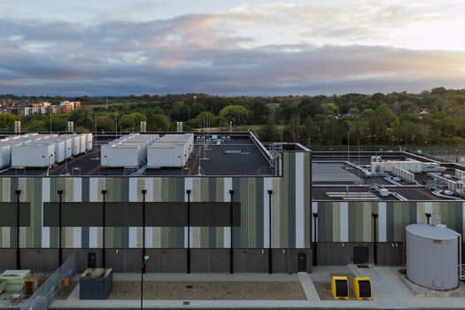 Aerial view of a modern data center building with rooftop cooling units and industrial architecture surrounded by lush greenery in the United Kingdom. Aerial view of a modern data center building with rooftop cooling units and industrial architecture surrounded by lush greenery in the United Kingdom.
