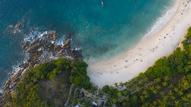 Aerial view of Freedom Beach featuring white sand turquoise waters and lush tropical vegetation along the rocky coastline in Tambon Patong Chang Wat Phuket Thailand.