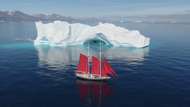 Aerial view of sailboat with red sails near iceberg Greenland. Aerial view of sailboat with red sails near iceberg Greenland.