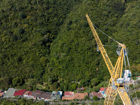 Aerial view of a large yellow construction crane positioned near a row of small houses with red roofs set against a dense green forest hillside in Istanbul Istanbul Turkiye. Aerial view of a large yellow construction crane positioned near a row of small houses with red roofs set against a dense green forest hillside in Istanbul Istanbul Turkiye.