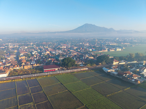 Kepanjen East Java Indonesia 28 August 2026 Aerial view of a train passing through Kepanjen surrounded by rice fields and buildings with a mountain in the distance.