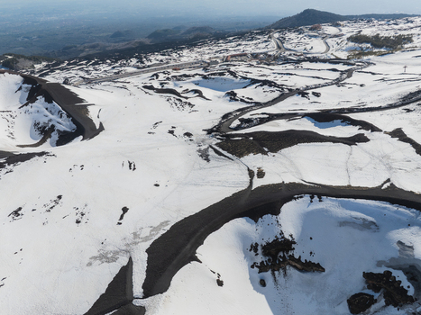 Aerial view of the snow covered south side of Mount Etna with winding mountain roads and dark volcanic craters in Nicolosi Sicilia Italy. Aerial view of the snow covered south side of Mount Etna with winding mountain roads and dark volcanic craters in Nicolosi Sicilia Italy.