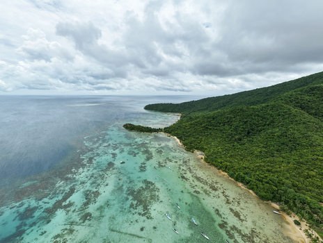 Aerial view of the serene Annora Beach where turquoise waters meet lush green hills under a vast cloudy sky Karimunjawa Jawa Tengah Indonesia.