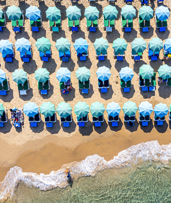 Aerial view of rows of turquoise and blue beach umbrellas and sunbeds on the sandy shore with people relaxing near the waves at Bat Yam beach in Bat Yam Center District Israel. Aerial view of rows of turquoise and blue beach umbrellas and sunbeds on the sandy shore with people relaxing near the waves at Bat Yam beach in Bat Yam Center District Israel.