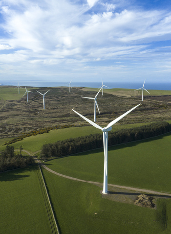 Aerial view of wind turbines standing on green fields and moorland overlooking the sea under a blue sky Scotland United Kingdom. Aerial view of wind turbines standing on green fields and moorland overlooking the sea under a blue sky Scotland United Kingdom.