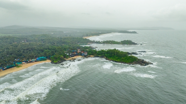 Aerial view of Palolem Beach with lush palm trees rocky headlands and waves crashing on the sandy shore in Canacona Goa India.