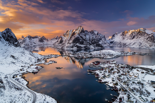 Aerial view of Reine village nestled among snow covered mountains and fjords under a golden sunset sky in Reine Nordland Norway. Aerial view of Reine village nestled among snow covered mountains and fjords under a golden sunset sky in Reine Nordland Norway.
