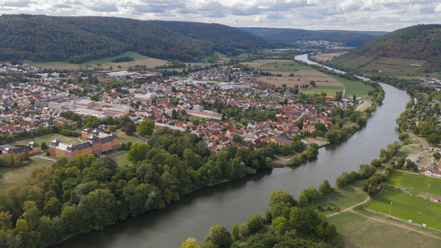 Aerial view of Kleinheubach town along the Main river featuring the historic Schloss Lowenstein lush forests and residential rooftops under a cloudy sky in Kleinheubach Bavaria Germany.