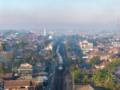 Kepanjen Indonesia 28 August 2026 Aerial view of a train passing through the town of Kepanjen with houses trees and a mosque visible under soft morning light.