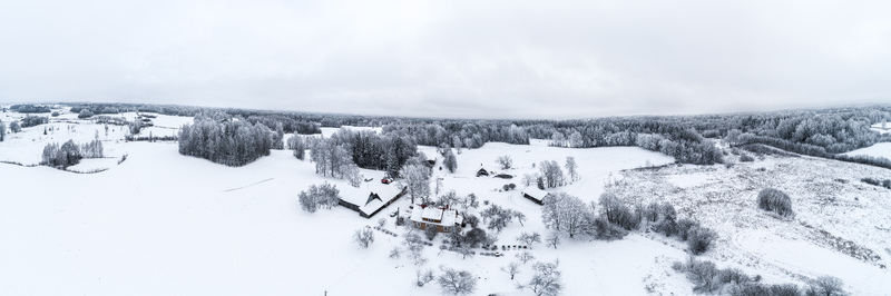Aerial view of a snow covered rural landscape featuring a farmhouse surrounded by frost laden trees and vast white fields in Latvia. Aerial view of a snow covered rural landscape featuring a farmhouse surrounded by frost laden trees and vast white fields in Latvia.