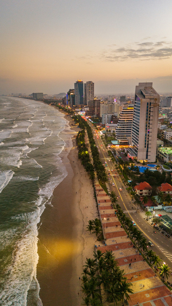 Aerial view of the coastline of Da Nang at sunset featuring modern high rise hotels a palm lined promenade and waves washing onto the sandy beach in Da Nang Vietnam. Aerial view of the coastline of Da Nang at sunset featuring modern high rise hotels a palm lined promenade and waves washing onto the sandy beach in Da Nang Vietnam.