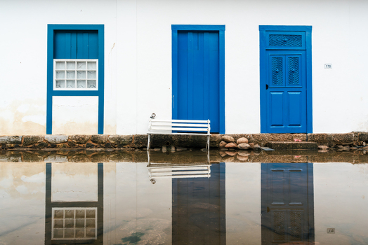 View of colonial architecture with vibrant blue doors and a white bench reflected in the flooded street of the historic center in Paraty State of Rio de Janeiro Brazil. View of colonial architecture with vibrant blue doors and a white bench reflected in the flooded street of the historic center in Paraty State of Rio de Janeiro Brazil.