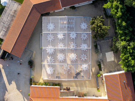 Aerial view of a transparent marquee tent set up for an outdoor event with round tables and chairs surrounded by historic buildings with terracotta roofs in Giao Porto Portugal.