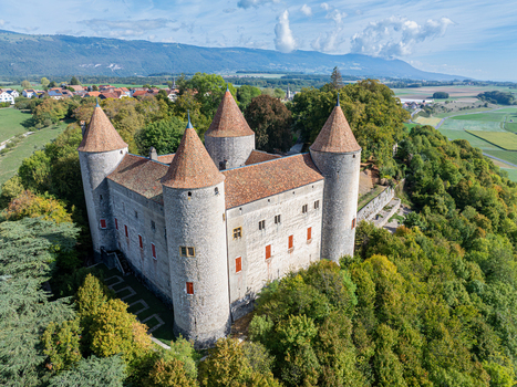 Aerial view of Champvent Castle with its stone walls and conical roofs surrounded by lush trees in the rural landscape of Champvent Vaud Switzerland. Aerial view of Champvent Castle with its stone walls and conical roofs surrounded by lush trees in the rural landscape of Champvent Vaud Switzerland.