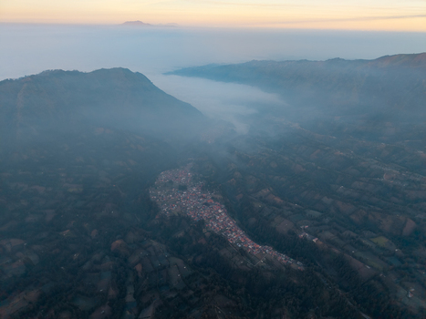 Aerial view of Wonotoro village nestled in a valley surrounded by misty mountains during sunset in Sukapura East Java Indonesia.